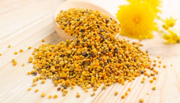 ranulki pyłku pszczelego na drewnianej łyżce i rozsypane na drewnianym blacie.