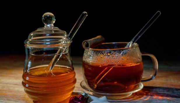 Słoik ciemnego miodu i filiżanka gorącej herbaty z drewnianą miodarką.